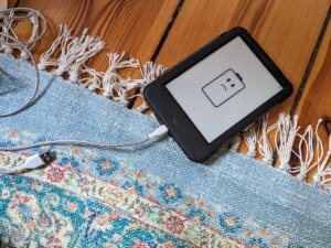 unhappy battery icon on Tolino eBook reader on a wooden floor half on a carpet